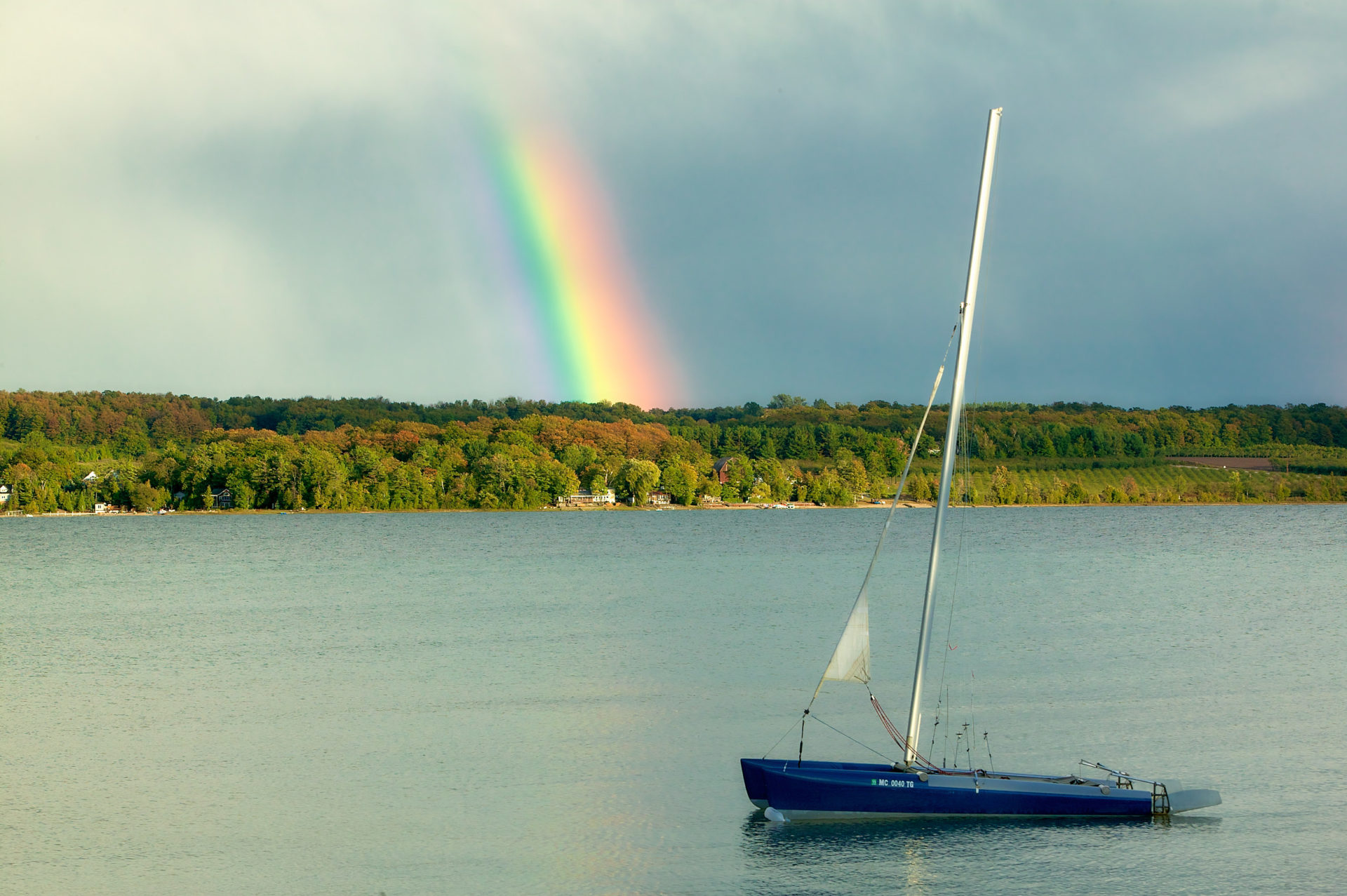rainbow leading into hillside over lake with Hobie cat anchored in foreground in Suttons Bay Michigan