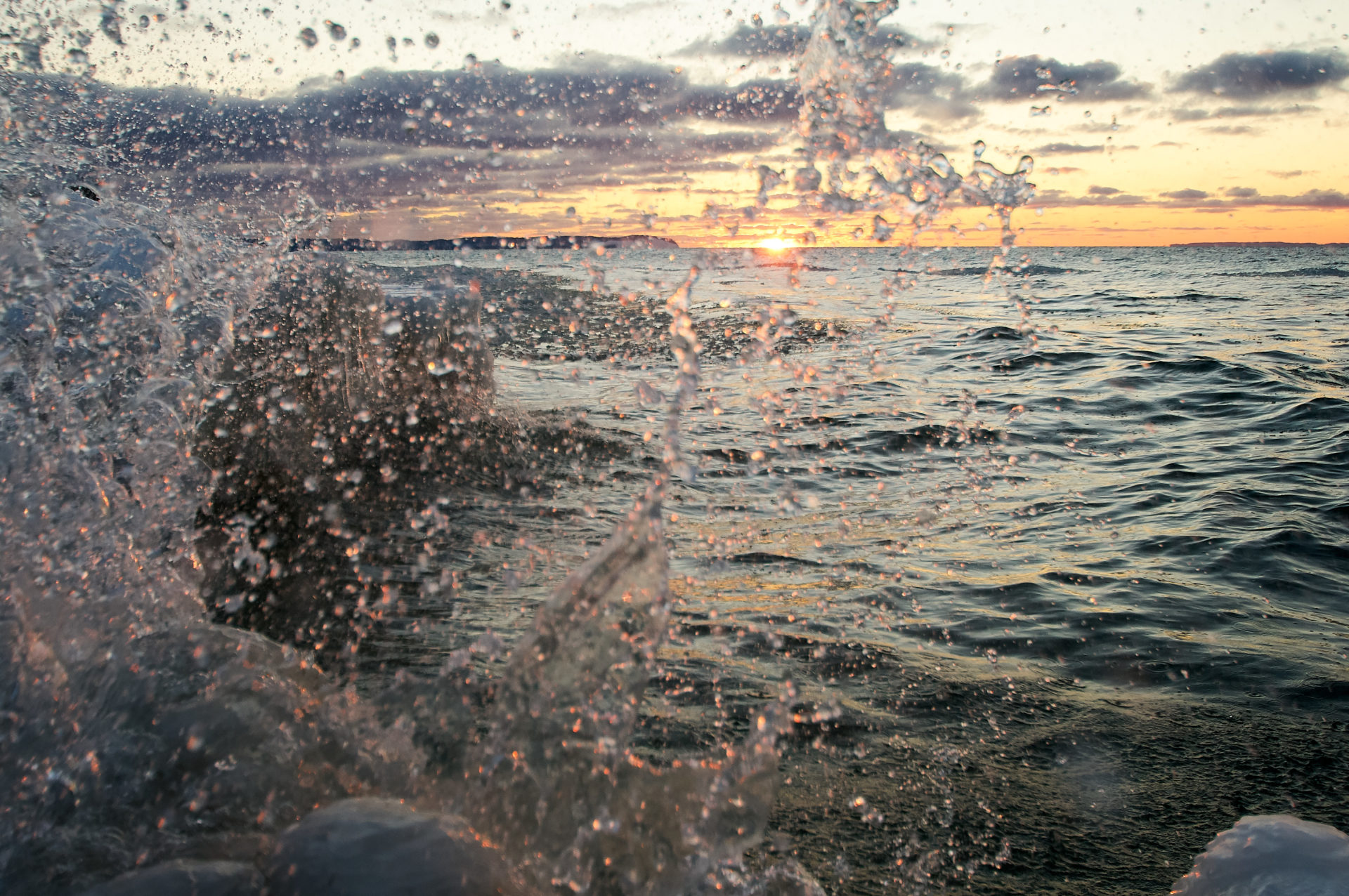 splashing water against shore ice during sunset at vans beach in Leland Michigan