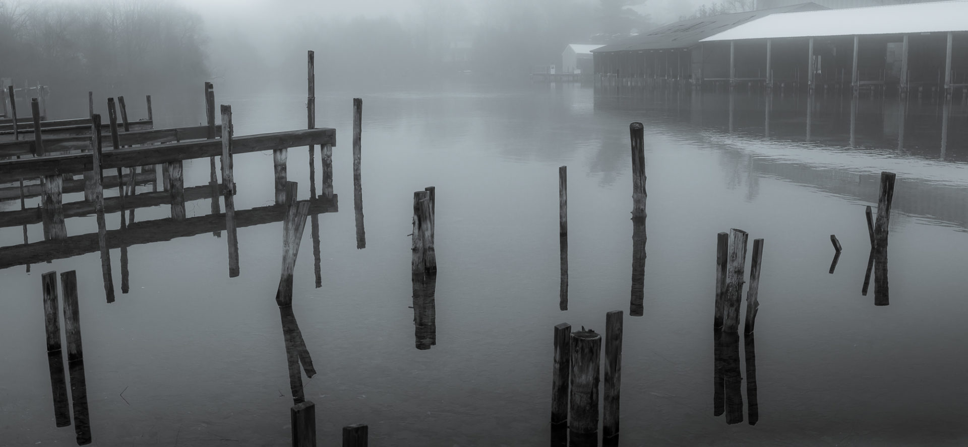 foggy morning looking over dock pilings and boathouse at standard marina on the carp river of Leland Michigan