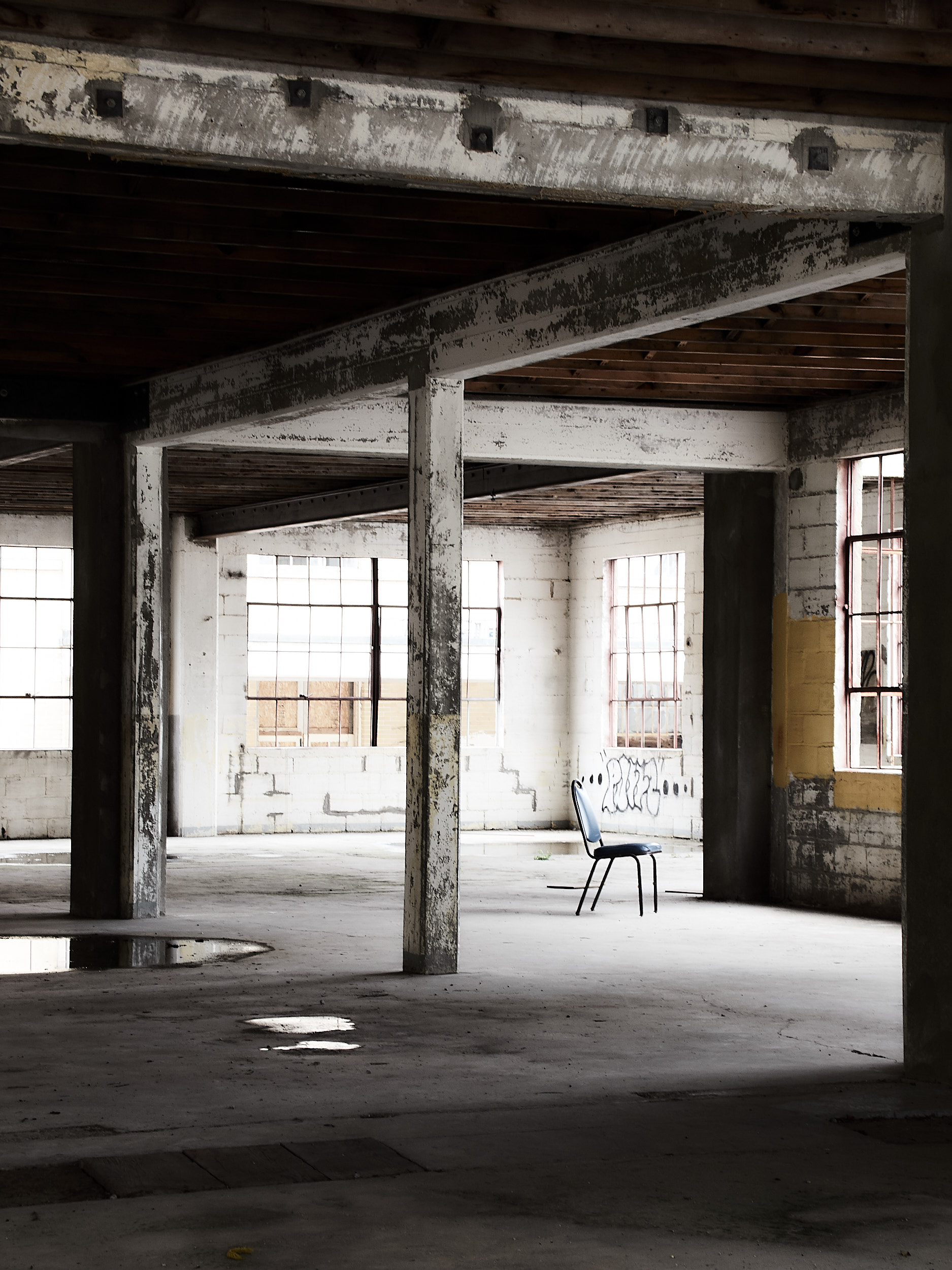 image of a chair sitting in an empty industrial space with light streaming in from the right edge of the frame