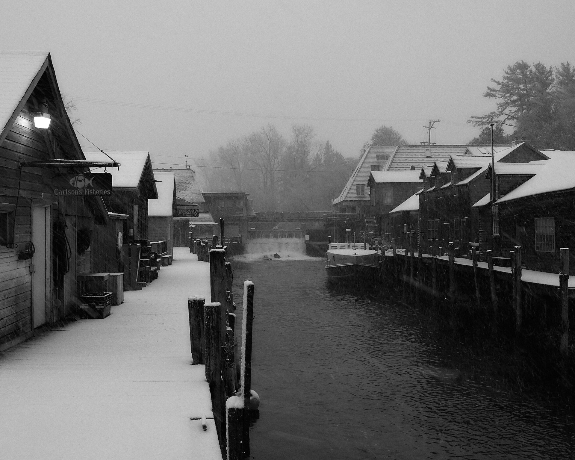 Fishtown Leland Michigan in the winter looking at the leland river dam, Carlsons fish market and the cove restaurant. light snow cover and the fishing boat Joy