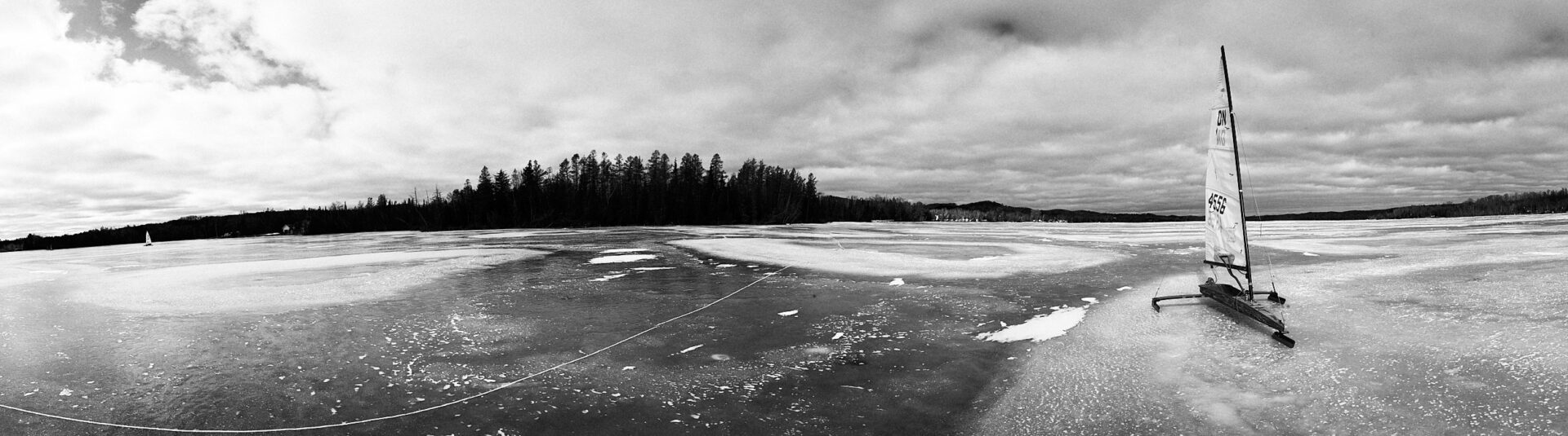 Monochrome panoramic image of dn iceboat sitting on the ice of south lake leelanau Michigan with cedar trees in the background